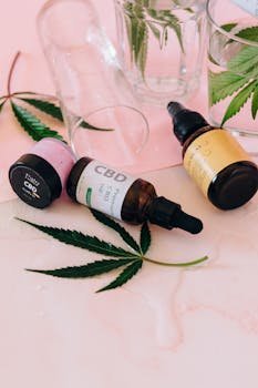 Aesthetic arrangement of CBD oil bottles with cannabis leaves on a pink background.